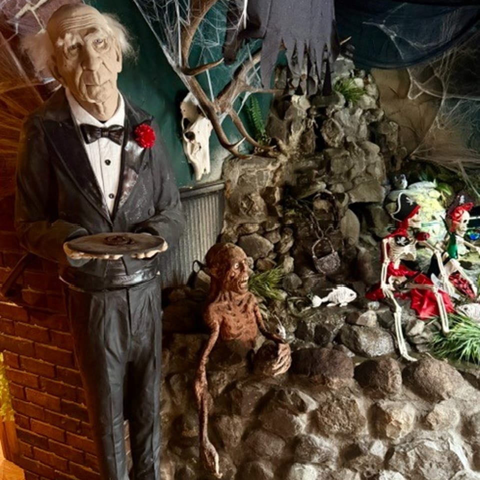 Halloween-themed restaurant display with a tuxedoed mannequin, cobwebs, skeletons, and a rocky haunted scene.