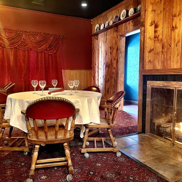 A cozy restaurant dining room with a set table, red velvet chairs, and a lit fireplace.