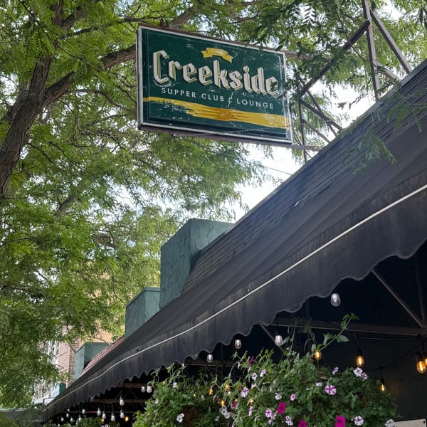 The Creekside Supper Club & Lounge sign hangs above a black awning with hanging flower baskets.