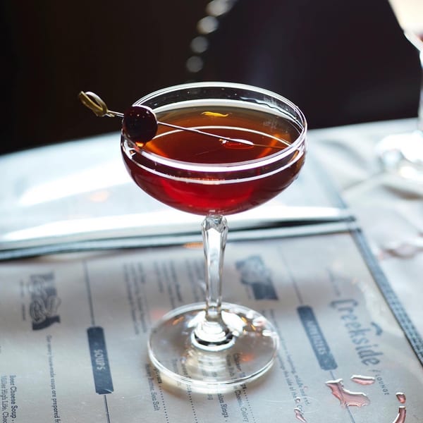 A red cocktail with a cherry garnish sits on a Creekside Lounge menu.