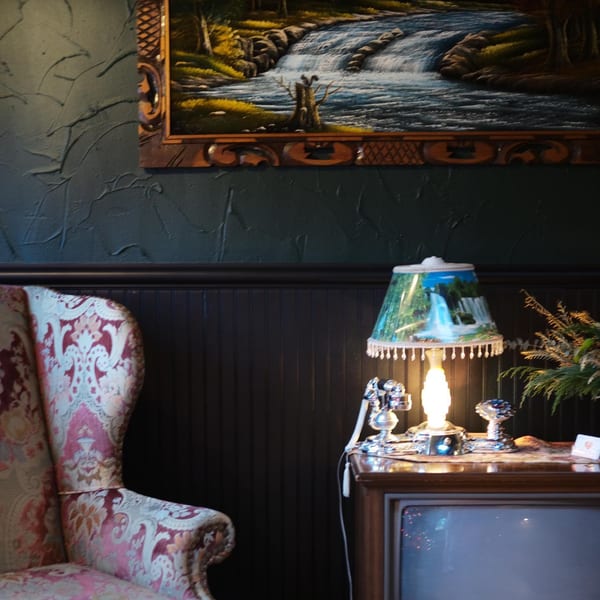 A patterned armchair, a lit lamp with a waterfall shade, and a vintage television set.