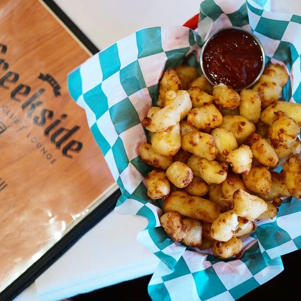 A basket of golden fried cheese curds with a side of dipping sauce next to a Creekside menu.