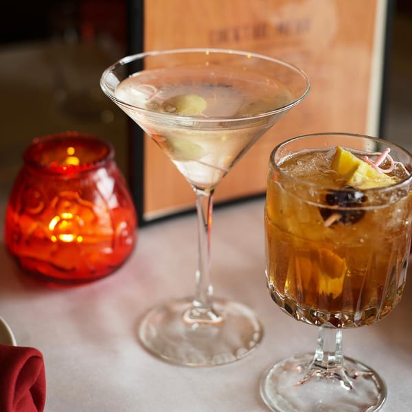 A martini, an old fashioned, and a red candle on a white tablecloth.