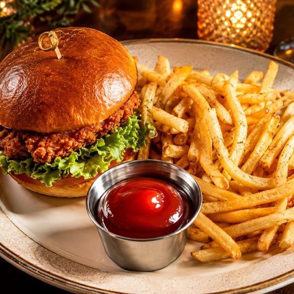 Crispy fried chicken sandwich with lettuce, tomato, and a side of golden french fries and ketchup.